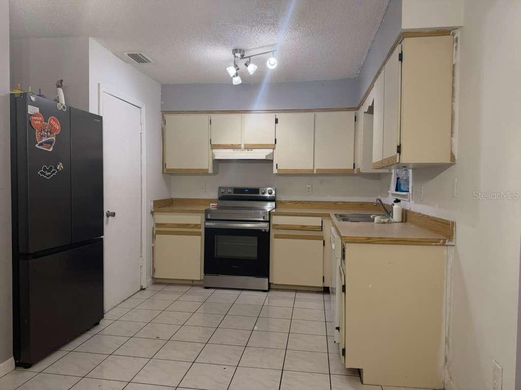 A kitchen with white cabinets, a black refrigerator, stainless steel stove, and tiled flooring — 2824 W HURON DRIVE, DELTONA, FL