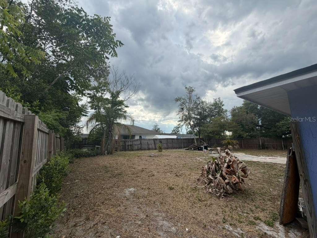 A fenced backyard features a patch of dry grass, some debris, and mature trees — 2824 W HURON DRIVE, DELTONA, FL