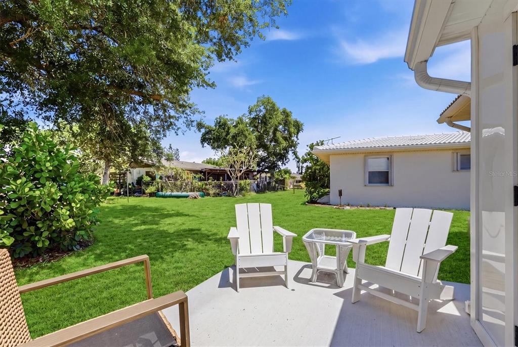A concrete patio with two white chairs overlooks a grassy backyard with mature trees — 8940 PICKWICK ROAD, NORTH PORT, FL