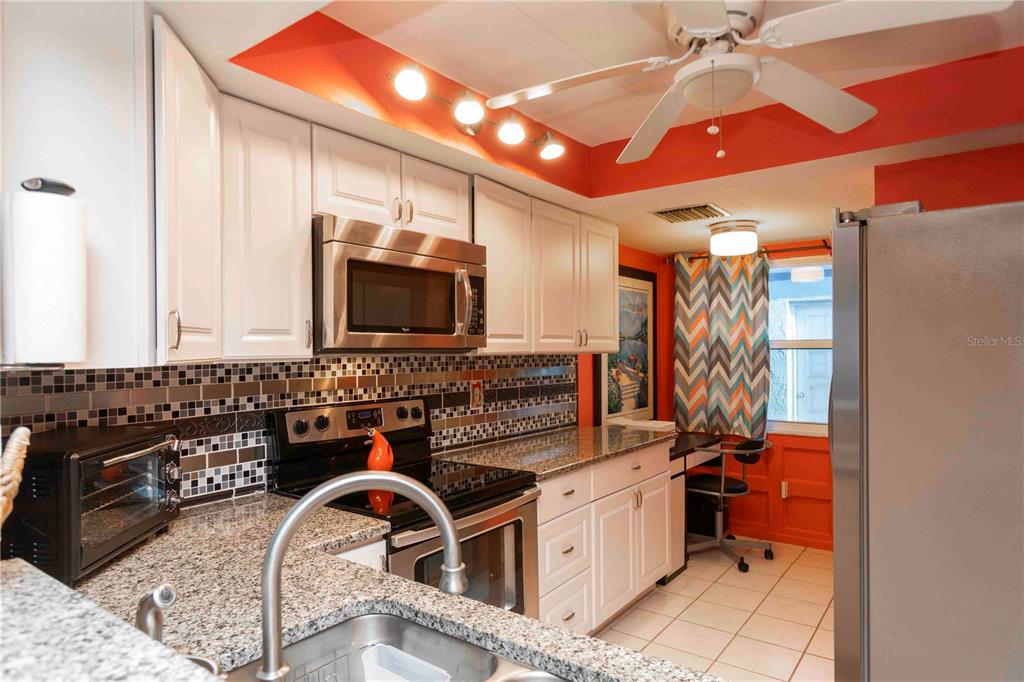 A kitchen features white cabinets, granite countertops, stainless steel appliances, and bright orange wall accents — 9639 GREENSKEEPER DRIVE UNIT 9639, NEW PORT RICHEY, FL