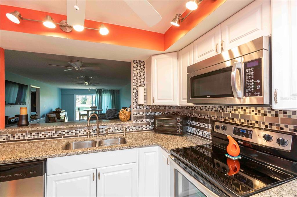 A kitchen with white cabinets, granite countertops, a mosaic tile backsplash, and stainless steel appliances — 9639 GREENSKEEPER DRIVE UNIT 9639, NEW PORT RICHEY, FL