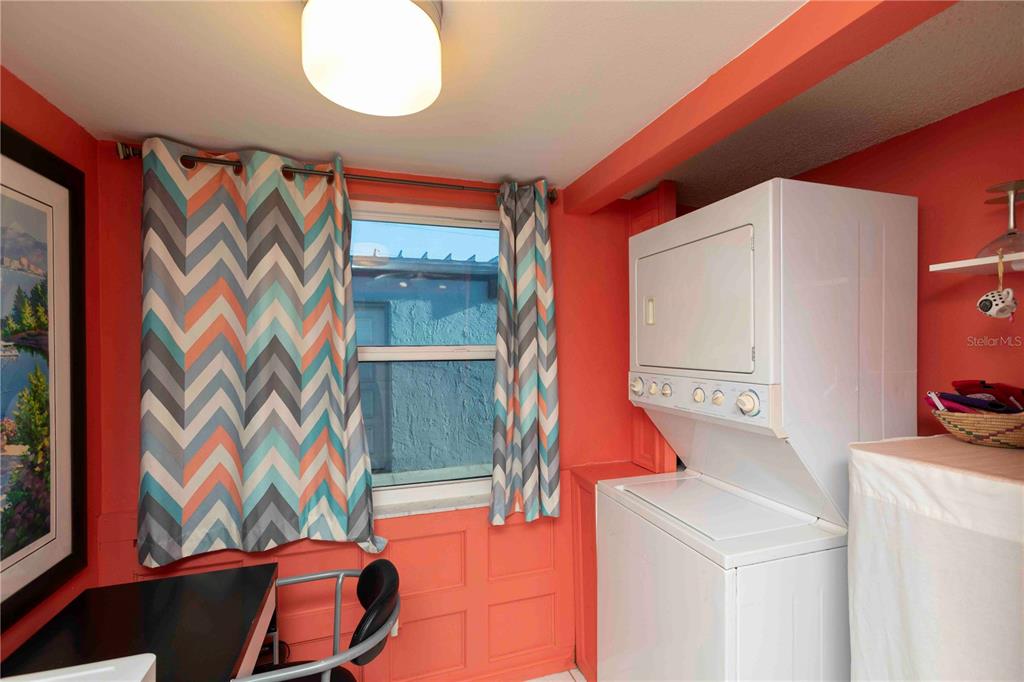 A laundry room features coral walls, a stacked washer and dryer, and patterned curtains — 9639 GREENSKEEPER DRIVE UNIT 9639, NEW PORT RICHEY, FL