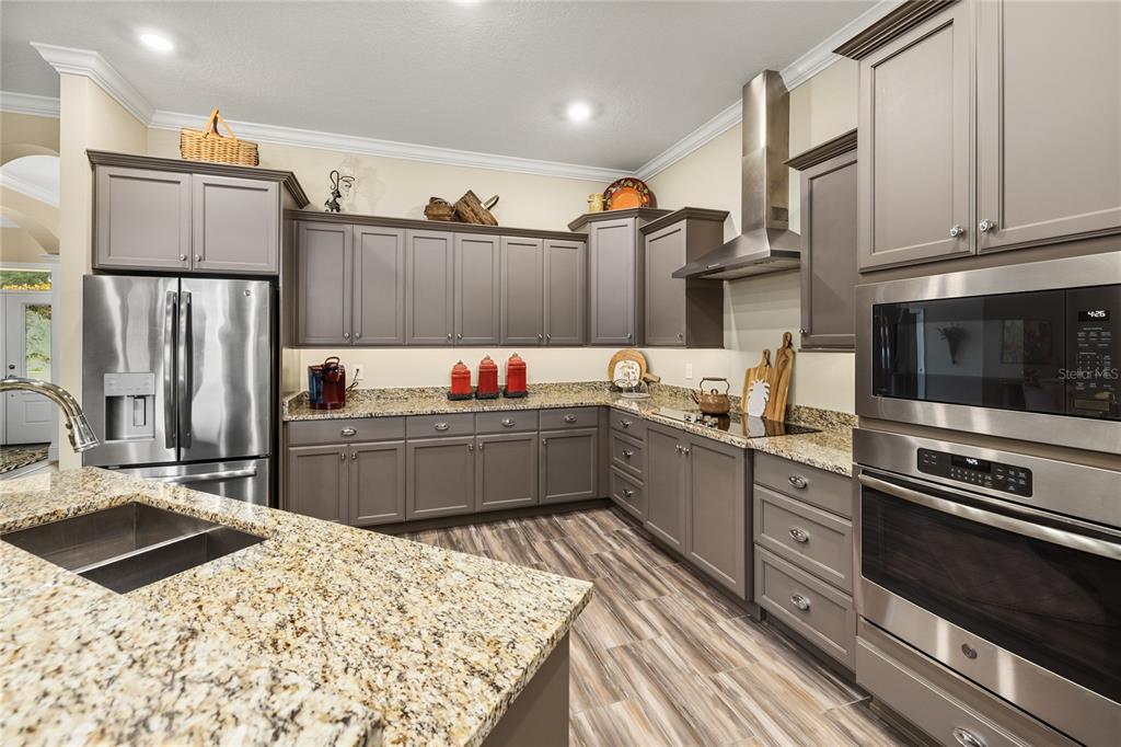 A kitchen features gray cabinets, granite countertops, stainless steel appliances, and wood-look flooring — 1097 SUGAR LOAF KEY LOOP, LADY LAKE, FL
