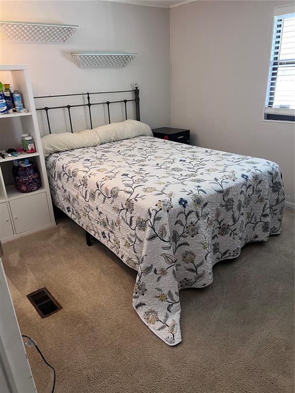 A bedroom features a metal-framed bed with a floral quilt, shelving, and carpeted flooring — 3326 DENISE DRIVE, ELLENTON, FL