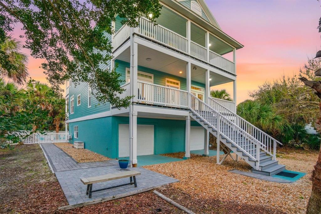 A three-story teal house with white trim, a large staircase, and a paved patio area — 9106 MELLON COURT, ST AUGUSTINE, FL
