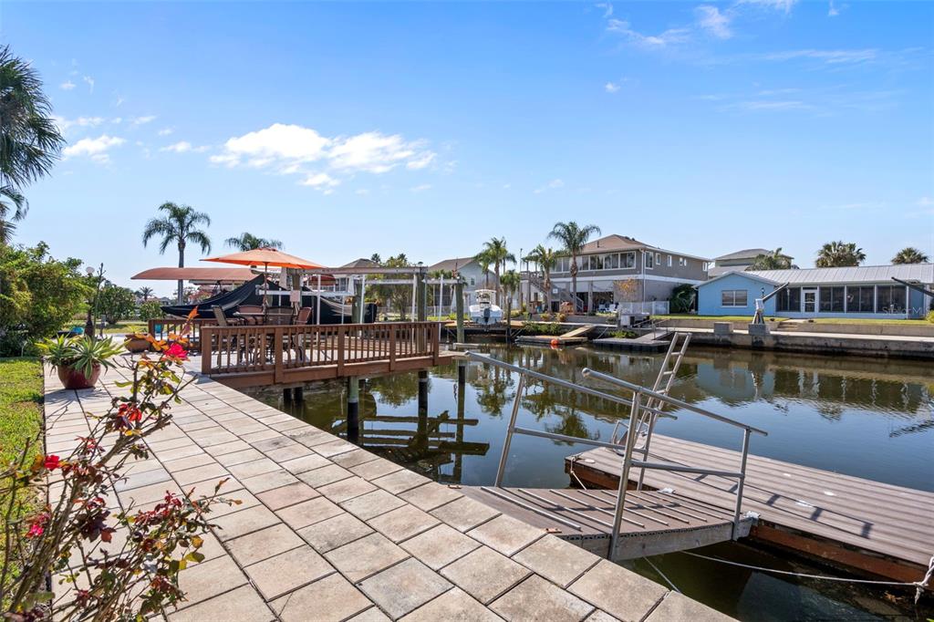 A paved patio overlooks a canal with a wooden deck and a floating boat dock — 15631 ALLMAND DRIVE, HUDSON, FL