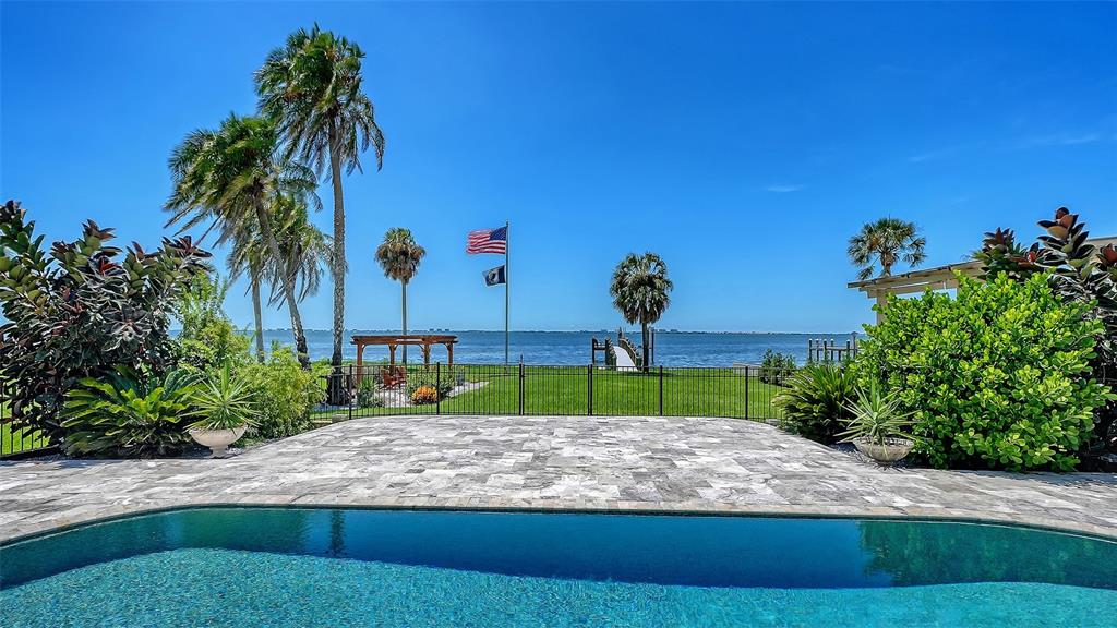 A swimming pool overlooks a grassy lawn, a wooden pergola, and a bay with palm trees — 7418 WESTMORELAND DRIVE, SARASOTA, FL