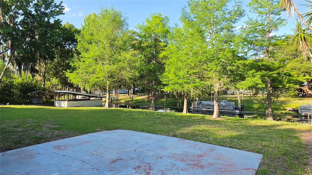 A concrete patio overlooks a grassy yard with trees, a boat slip, and a pontoon boat — 33 MAIN STREET, WINDERMERE, FL