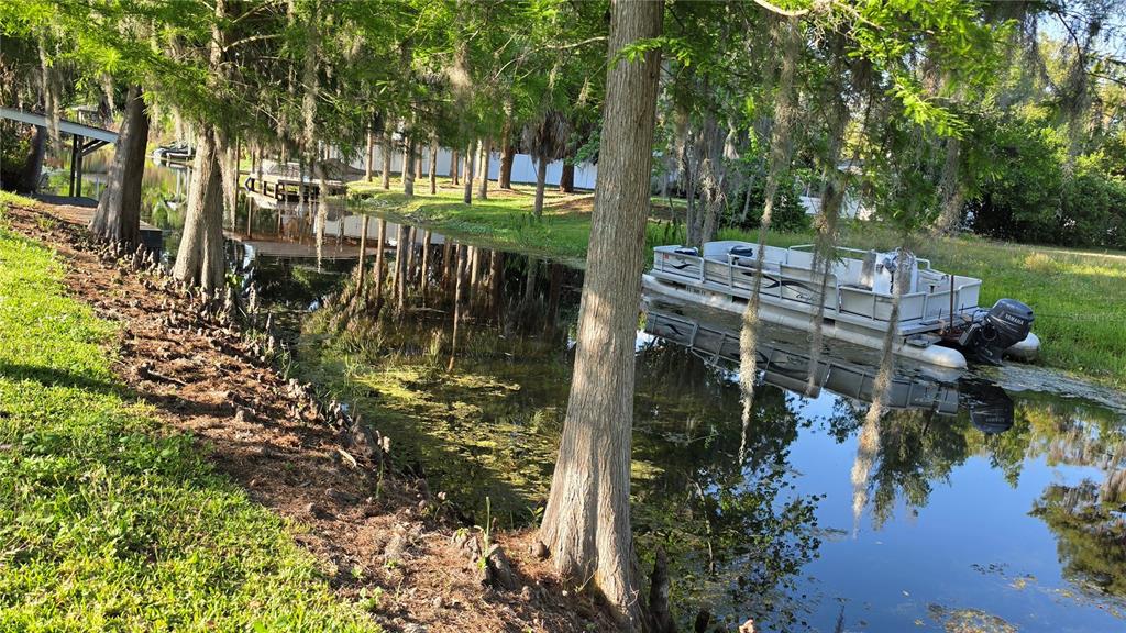 A pontoon boat is docked in a narrow canal lined with cypress trees and moss — 33 MAIN STREET, WINDERMERE, FL