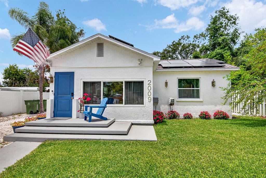 A white single-story house features a blue front door, solar panels, and a front lawn — 2009 1ST AVENUE E, BRADENTON, FL