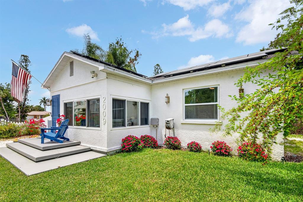 A white house exterior with a blue front door, a small porch, and red flowers — 2009 1ST AVENUE E, BRADENTON, FL
