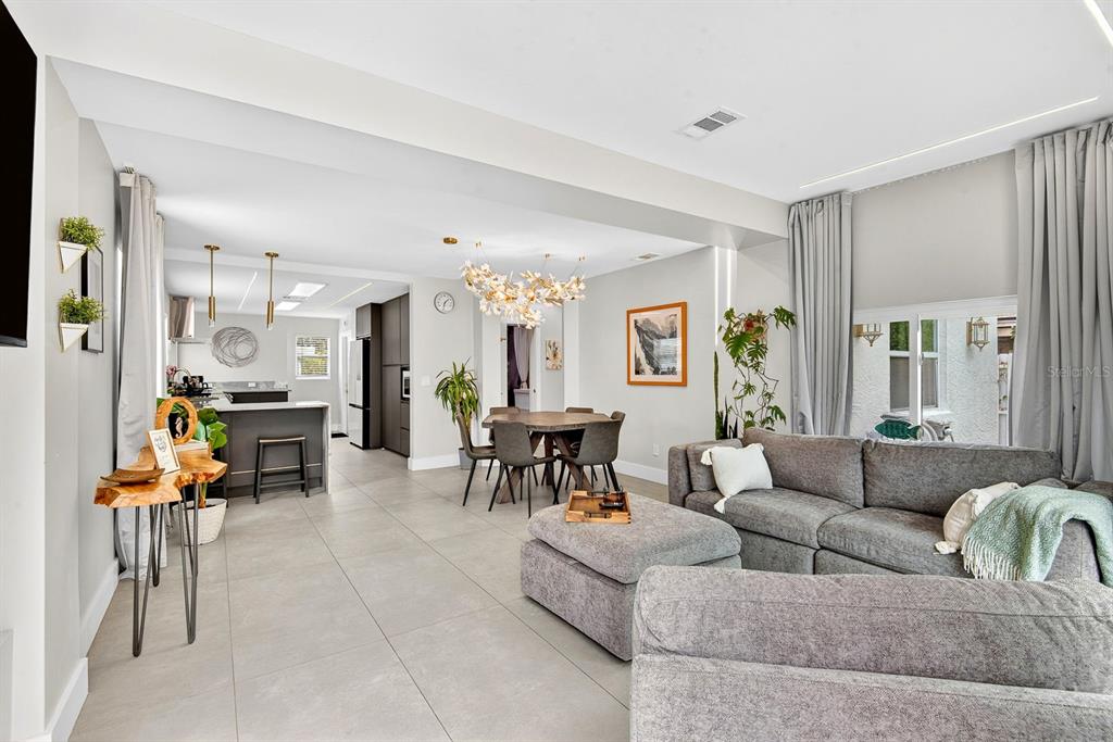 An open-concept living and dining area features gray tile flooring and a modern chandelier — 2009 1ST AVENUE E, BRADENTON, FL