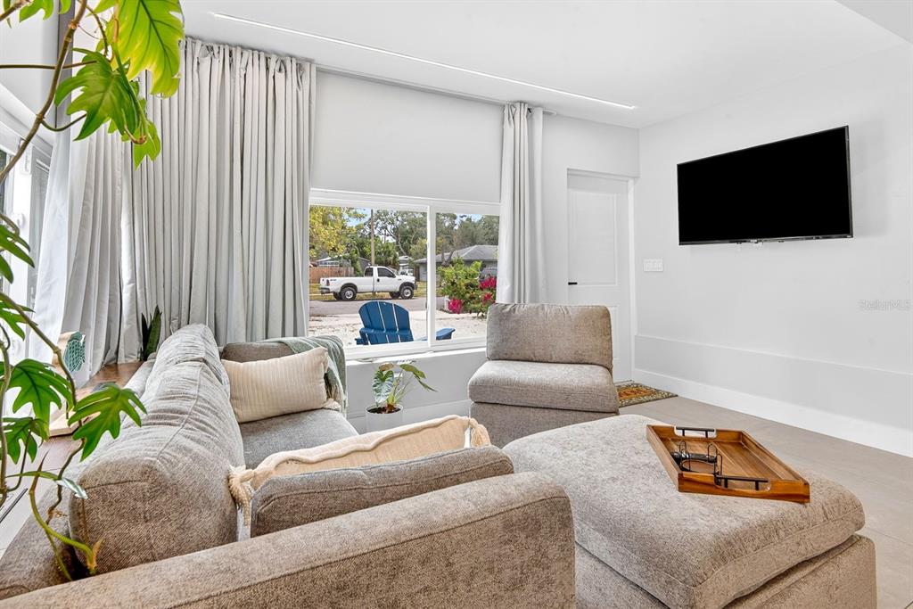 A living room features a grey sectional sofa, an armchair, a television, and large windows — 2009 1ST AVENUE E, BRADENTON, FL
