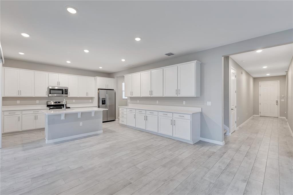 A modern kitchen features white cabinets, a central island, and light-colored wood-look tile flooring — 686 HERITAGE SQUARE DRIVE, HAINES CITY, FL
