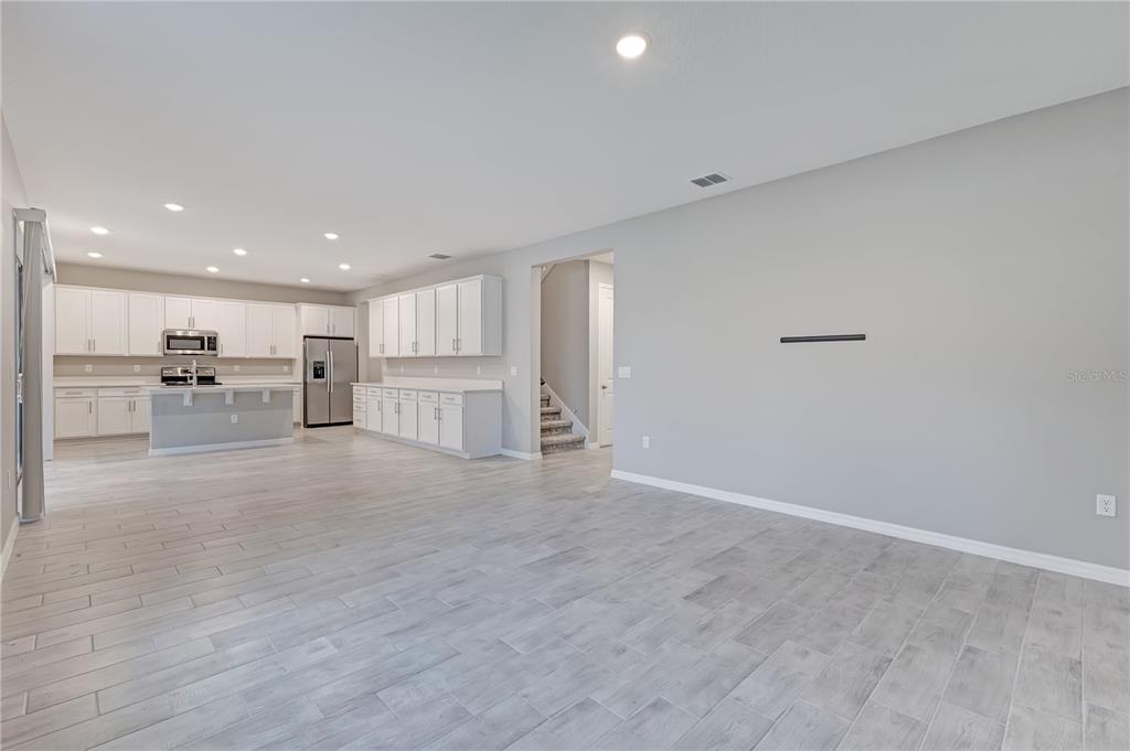 An open-concept kitchen and living area feature white cabinetry, stainless appliances, and gray tile flooring — 686 HERITAGE SQUARE DRIVE, HAINES CITY, FL