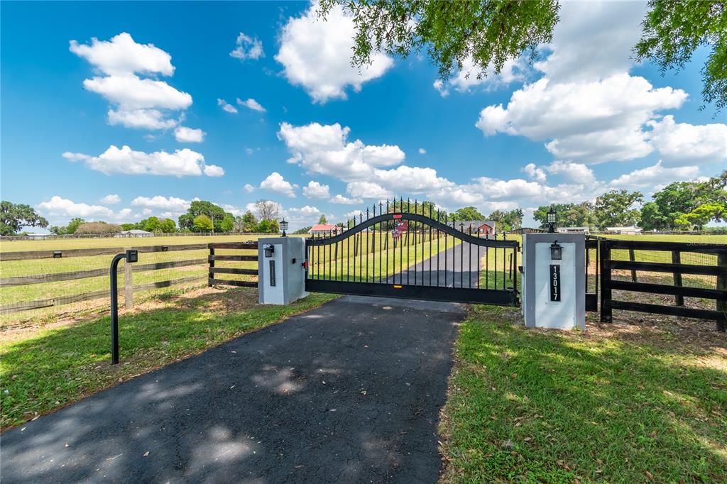 A black metal gate stands at the entrance of a paved driveway on a property — 13025 NW GAINESVILLE ROAD, REDDICK, FL
