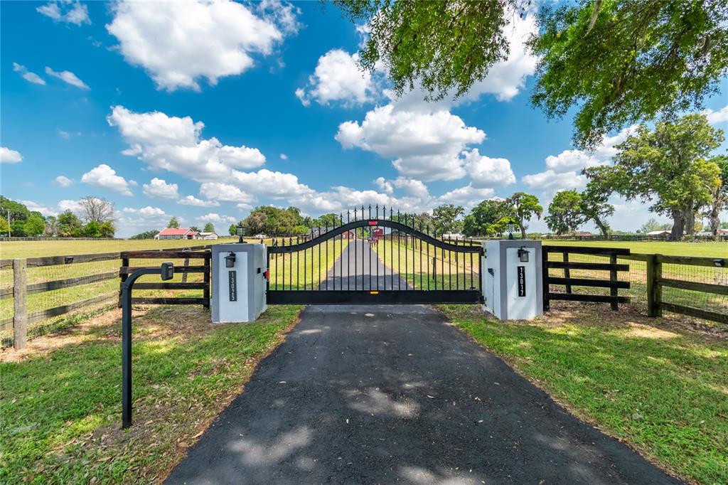 A black metal gate stands between two white pillars at the entrance of a driveway — 13025 NW GAINESVILLE ROAD, REDDICK, FL