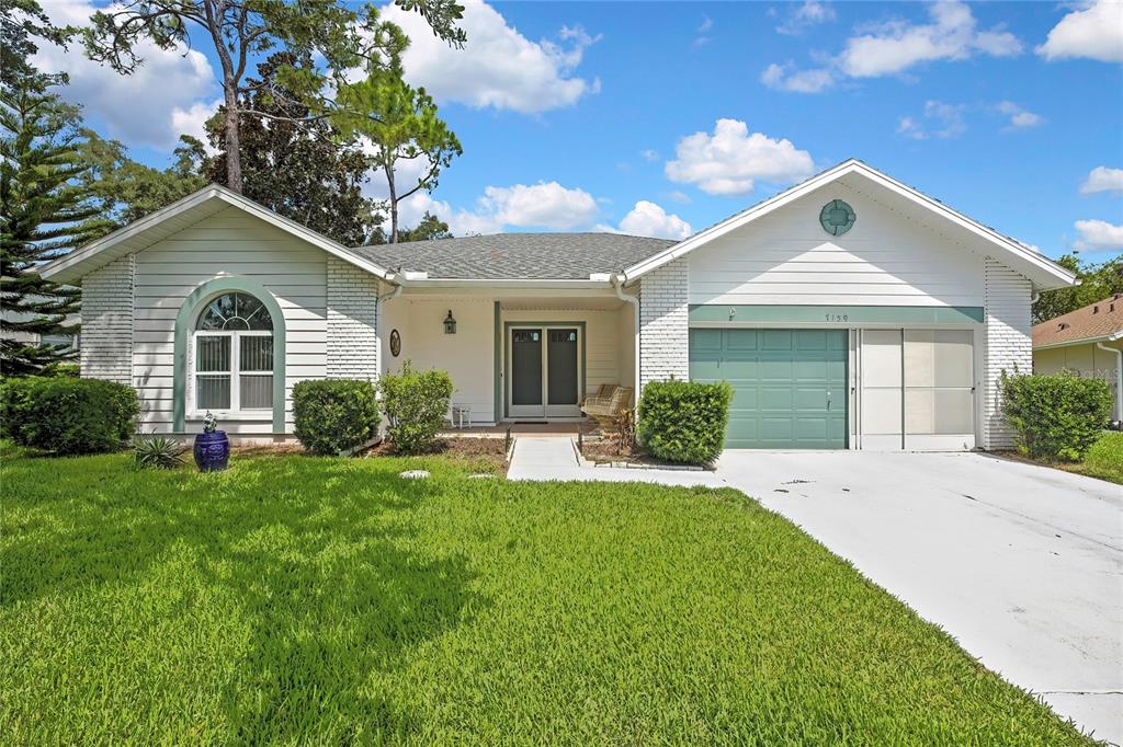 A single-story house with white siding, a green garage door, and a front lawn — 7159 CROWN OAKS DRIVE, SPRING HILL, FL