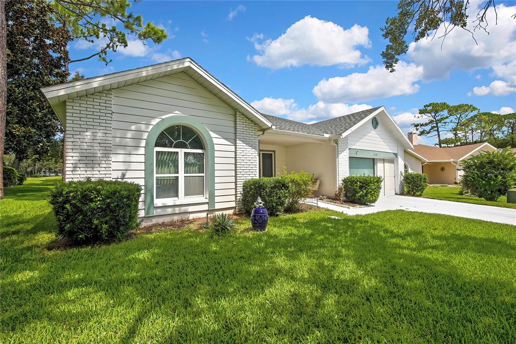 A single-story house with white siding, brick accents, and a front lawn under a blue sky — 7159 CROWN OAKS DRIVE, SPRING HILL, FL