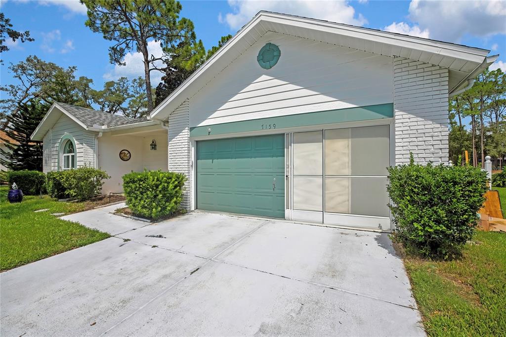 A single-story house with a teal garage door, white brick siding, and a concrete driveway — 7159 CROWN OAKS DRIVE, SPRING HILL, FL
