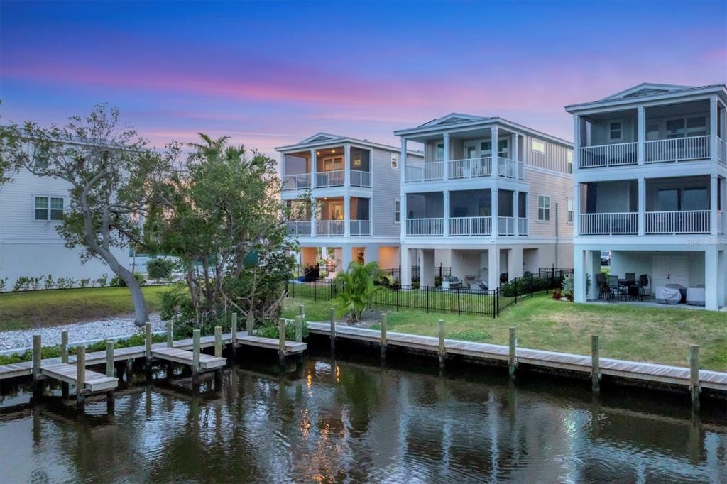 Three elevated waterfront houses with screened balconies stand along a canal with wooden docks — 4357 MARINA VIEW WAY, CORTEZ, FL