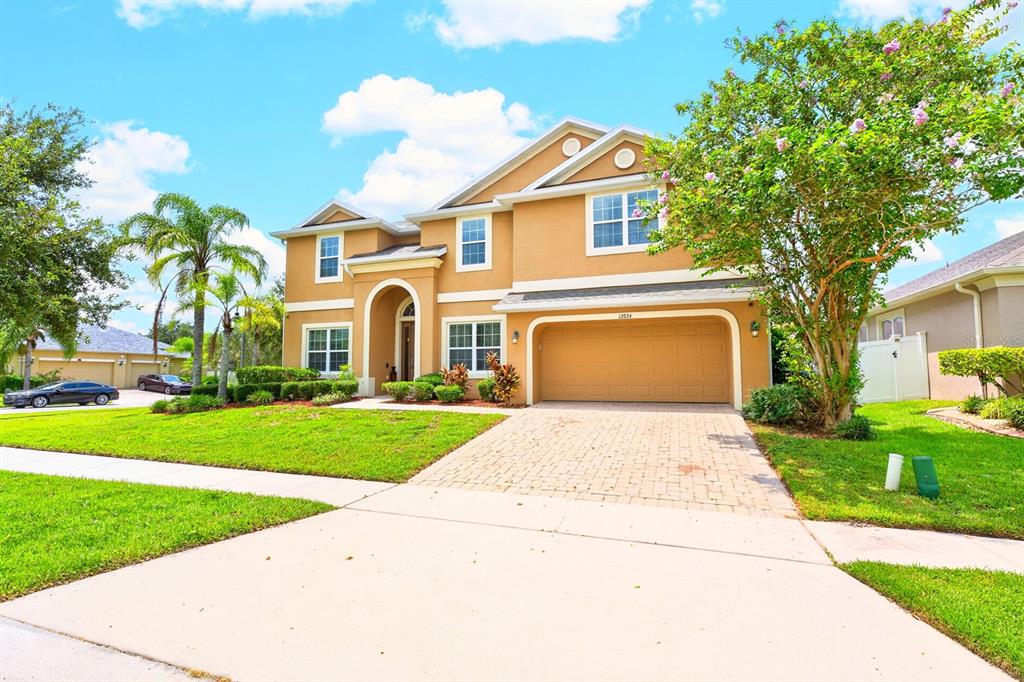 A two-story tan house with a paved driveway, a two-car garage, and a front lawn — 12834 BOGGY VIEW DRIVE, ORLANDO, FL