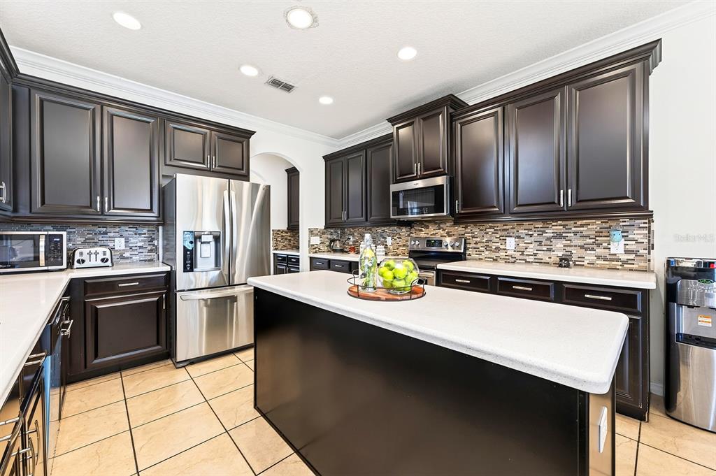 A kitchen features dark wood cabinets, stainless steel appliances, a central island, and tiled flooring — 12834 BOGGY VIEW DRIVE, ORLANDO, FL