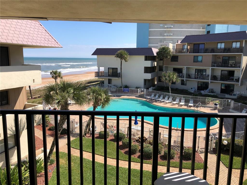 A balcony view overlooks a swimming pool, palm trees, and the ocean beach — 935 OCEAN SHORE BOULEVARD UNIT 3040, ORMOND BEACH, FL