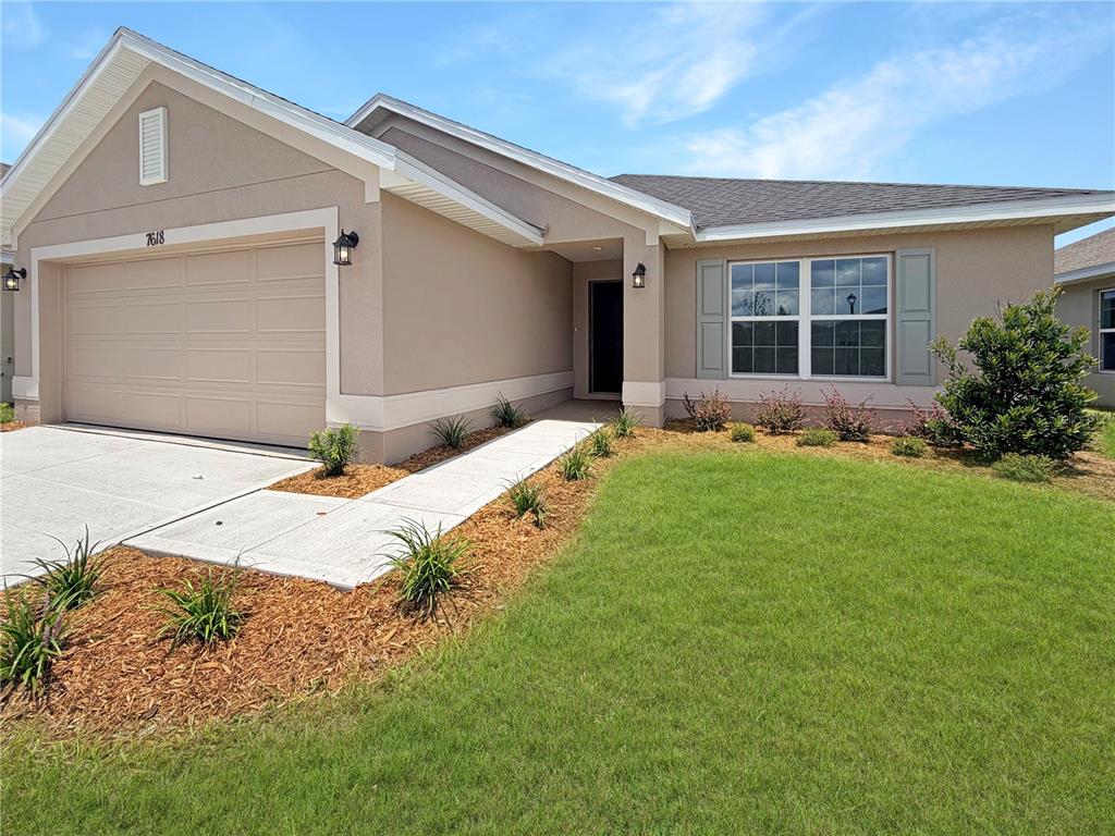 A single-story house with a beige stucco exterior, a two-car garage, and a front walkway — 7618 BENT TREE LOOP, HARMONY, FL