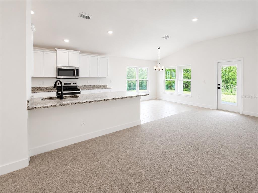 A kitchen with white cabinets and granite countertops overlooks a carpeted living area — 7618 BENT TREE LOOP, HARMONY, FL