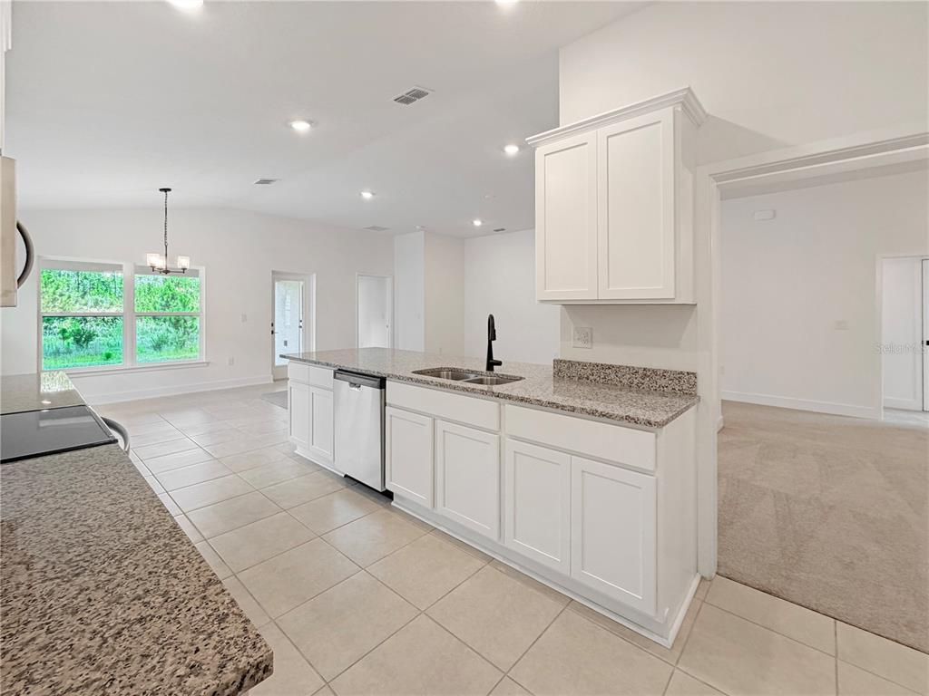 A kitchen features white cabinets, granite countertops, a stainless steel dishwasher, and tile flooring — 7618 BENT TREE LOOP, HARMONY, FL