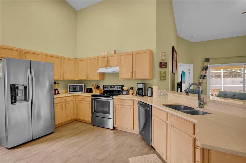 A kitchen features light wood cabinets, stainless steel appliances, and a double sink on a peninsula — 1208 CEDARWOOD WAY, CLERMONT, FL
