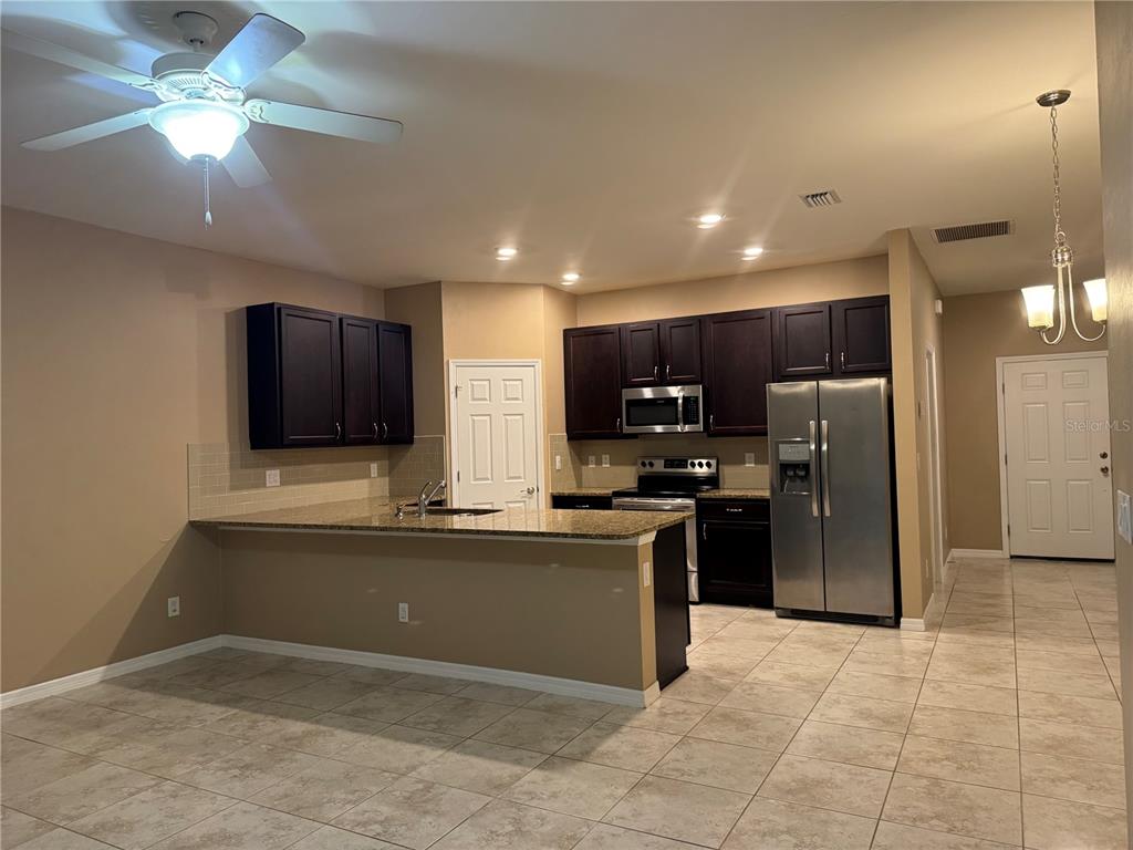 A kitchen features dark wood cabinets, granite countertops, stainless steel appliances, and tile flooring — 26077 SANDHILL BOULEVARD, PUNTA GORDA, FL
