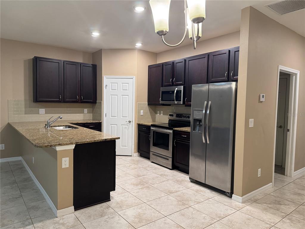 A kitchen features dark wood cabinets, granite countertops, stainless steel appliances, and beige tile flooring — 26077 SANDHILL BOULEVARD, PUNTA GORDA, FL