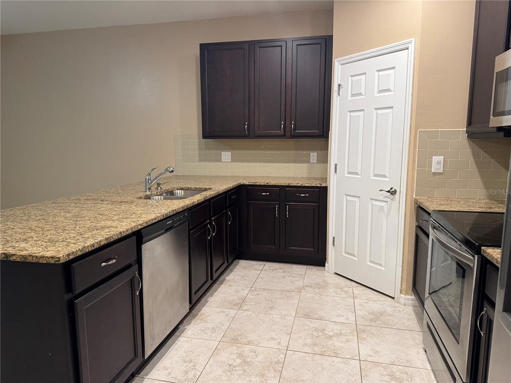 A kitchen features dark wood cabinets, granite countertops, stainless steel appliances, and beige tile flooring — 26077 SANDHILL BOULEVARD, PUNTA GORDA, FL