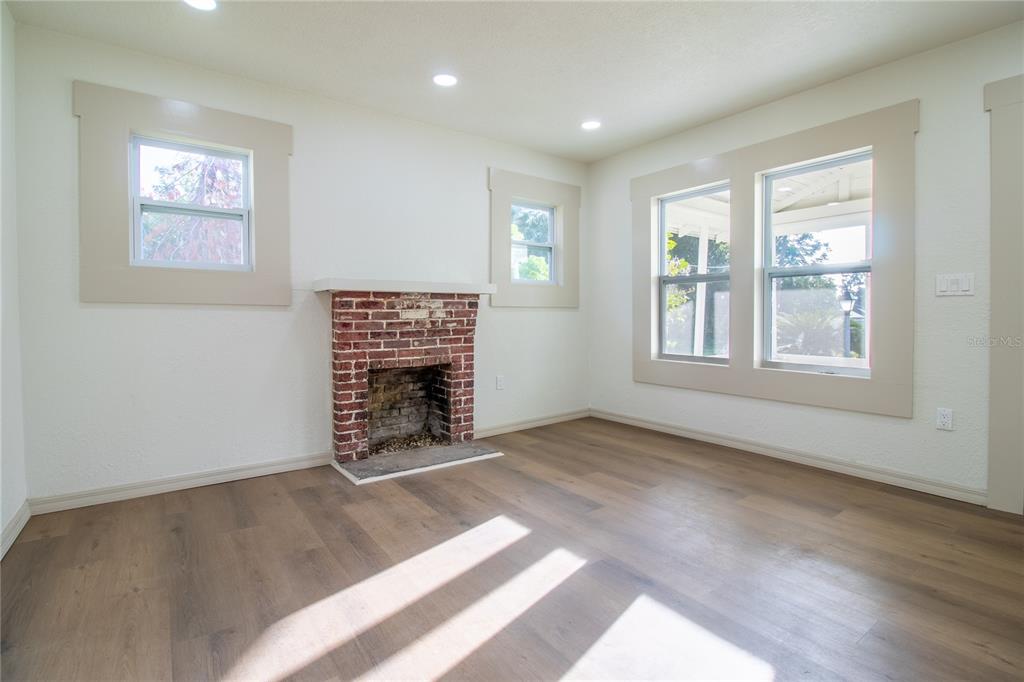 A living room features a brick fireplace, light wood-look flooring, and white walls — 14022 4TH STREET, DADE CITY, FL