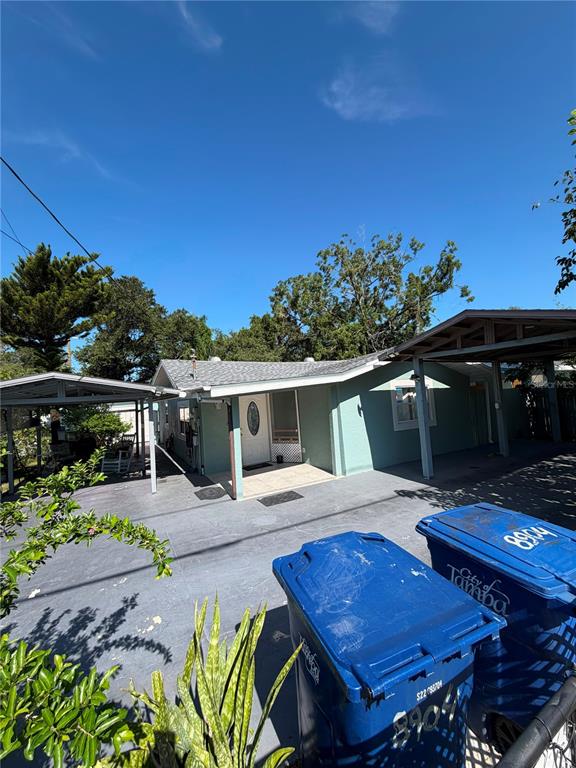 A light green house with a covered carport and two blue trash bins in the driveway — 8904 N 20TH STREET, TAMPA, FL