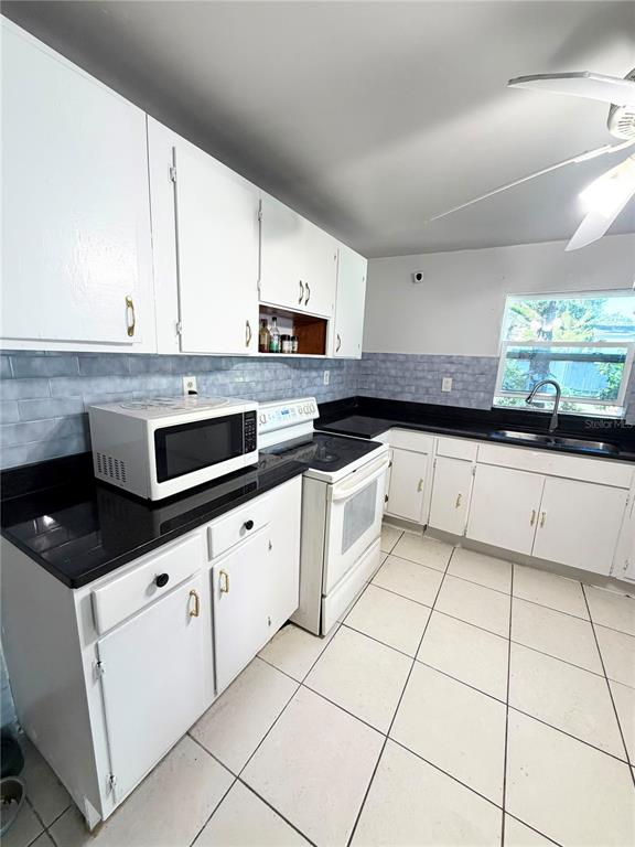 A kitchen features white cabinets, black countertops, a microwave, a white stove, and tiled floors — 8904 N 20TH STREET, TAMPA, FL