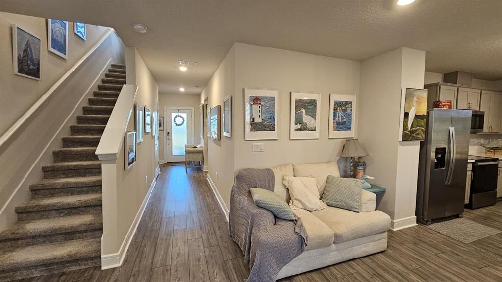 A hallway with a staircase, a sofa, and a kitchen area with stainless steel appliances — 8323 REEFBAY COVE, PARRISH, FL