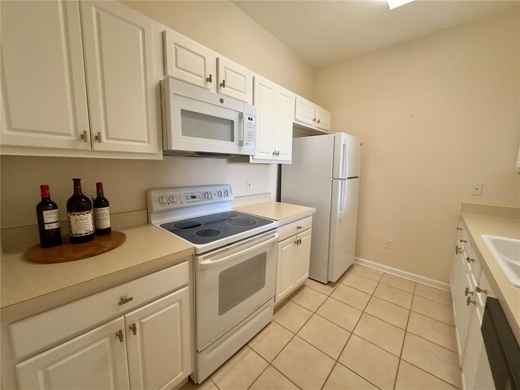 A kitchen features white cabinets, white appliances, beige countertops, and light-colored tile flooring — 13536 TURTLE MARSH LOOP UNIT 532, ORLANDO, FL