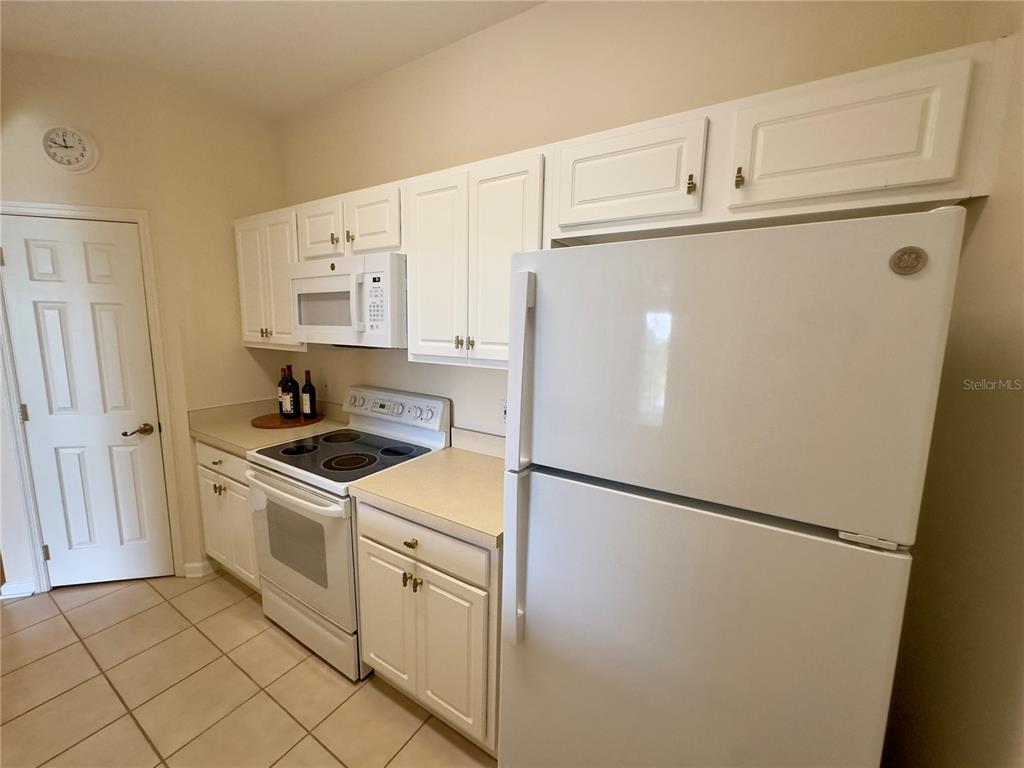 A kitchen features white cabinets, white appliances, tiled flooring, and a door on the left — 13536 TURTLE MARSH LOOP UNIT 532, ORLANDO, FL