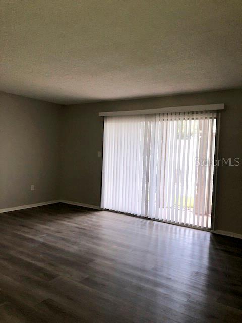 An empty room with gray walls, wood-look flooring, and vertical blinds covering a sliding door — 548 ORANGE DRIVE UNIT 14, ALTAMONTE SPRINGS, FL