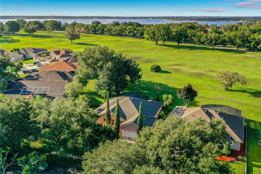 An aerial view of suburban houses bordering a large, open green field and a lake — 9833 SPRING LAKE DRIVE, CLERMONT, FL