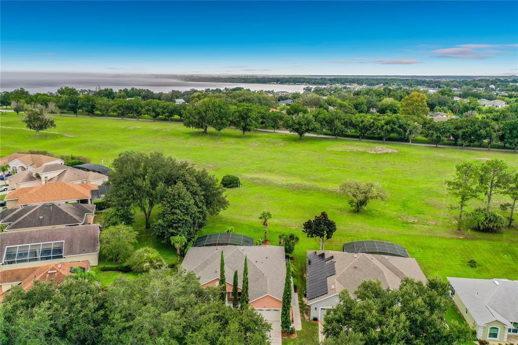 An aerial view shows suburban houses with screened pools bordering a large, open grassy field — 9833 SPRING LAKE DRIVE, CLERMONT, FL