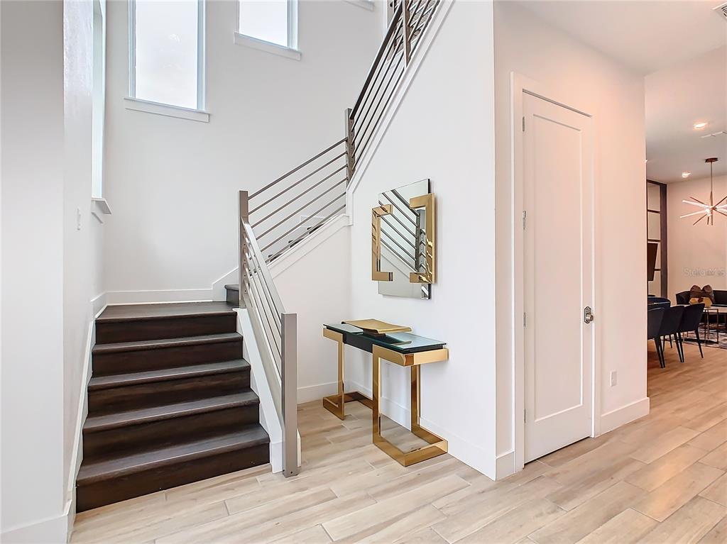 A staircase with dark wood treads and a metal railing sits beside a gold console table — 2125 PINE OAK LOOP, DAVENPORT, FL