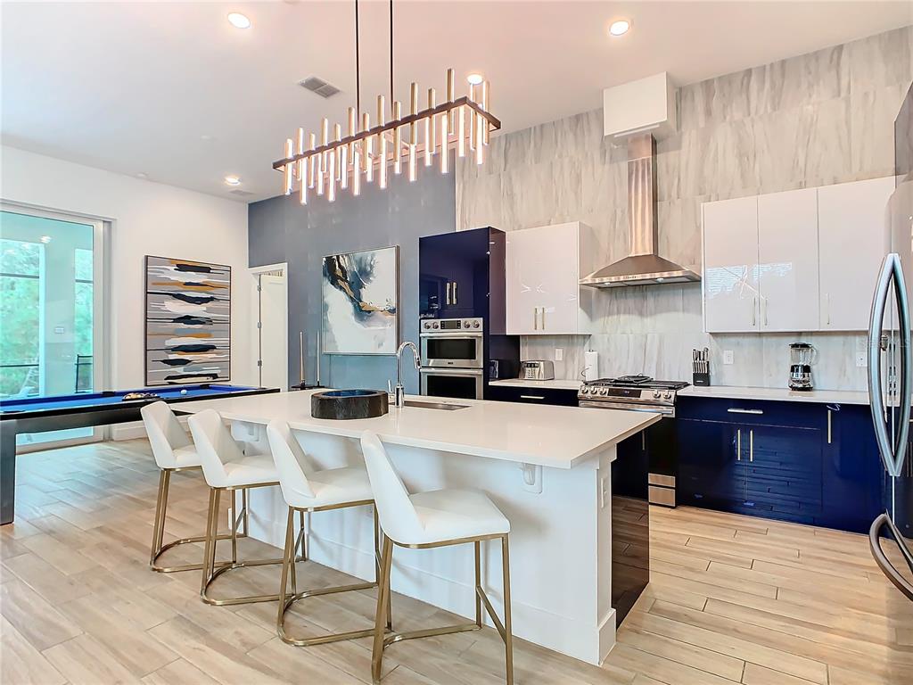 A modern kitchen features a large white island, blue cabinetry, and a pool table nearby — 2125 PINE OAK LOOP, DAVENPORT, FL
