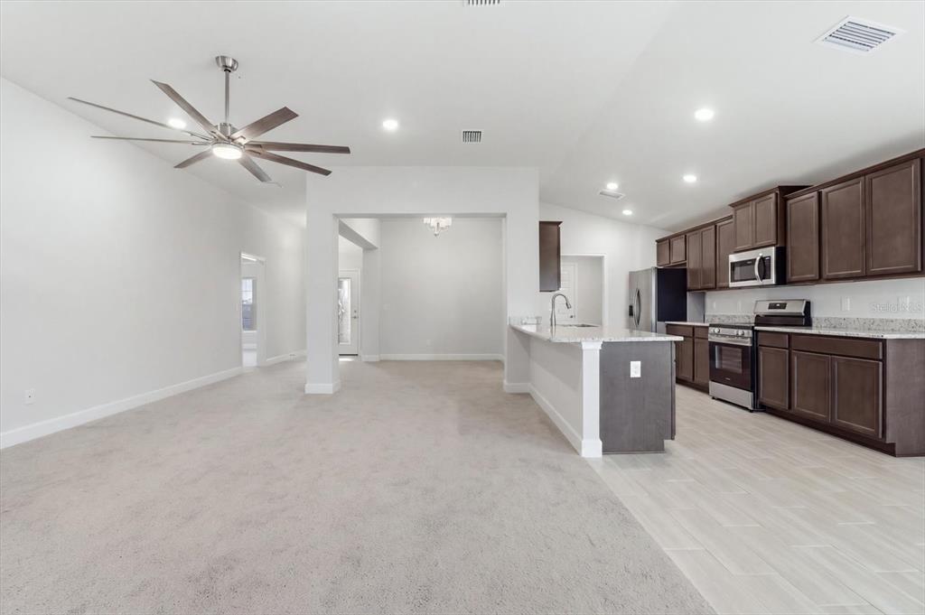 An open-concept kitchen with dark wood cabinets and a carpeted living area with a fan — 336 W REXFORD DRIVE, BEVERLY HILLS, FL