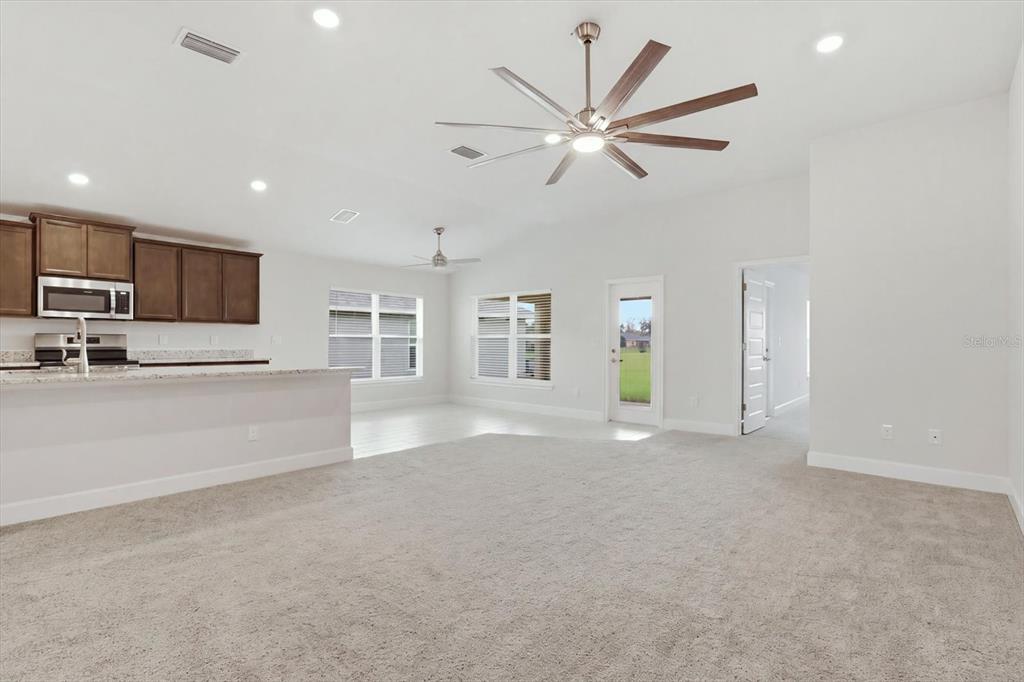 A spacious living room with beige carpeting, a large ceiling fan, and an open kitchen — 336 W REXFORD DRIVE, BEVERLY HILLS, FL