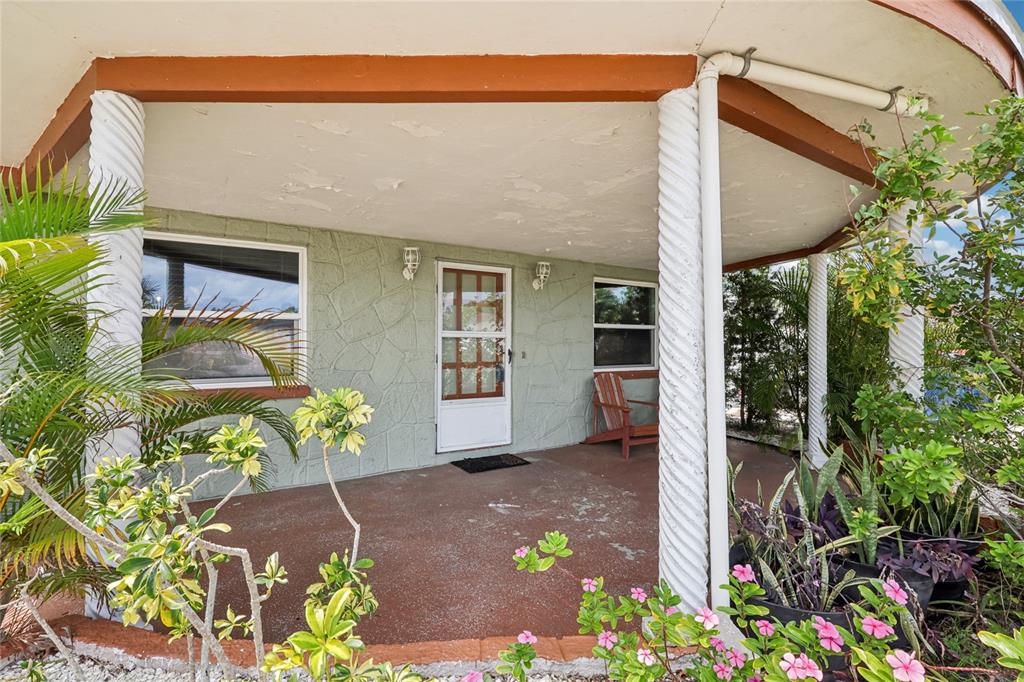 A covered porch features a light green stone-patterned wall, white spiral columns, and a door — 3548 DARLINGTON ROAD, HOLIDAY, FL