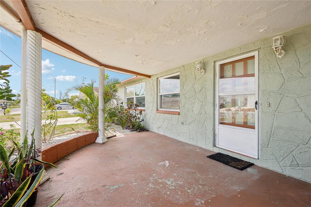 A covered front porch with a concrete floor, white columns, and light green stone-patterned siding — 3548 DARLINGTON ROAD, HOLIDAY, FL